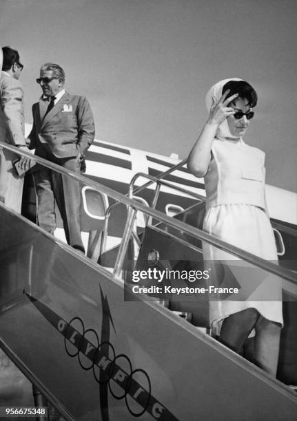 La cantatrice Maria Callas descendant une passerelle d'avion, derrière elle Aristote Onassis.