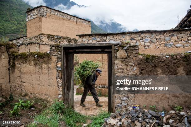 This picture taken on April 23, 2018 shows villager carrying food for his livestock past devastated houses in the old village of Luobozhai , which...