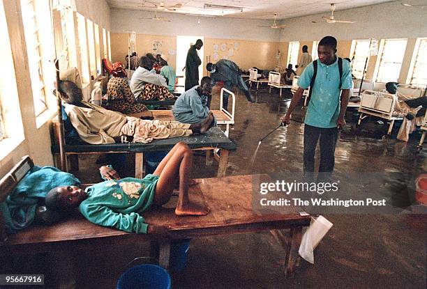 Mutari Mustapha lies sick from Cholera while at right hospital staffer Victor Momah sprays a chlorine-based solution to disinfect the area around him.
