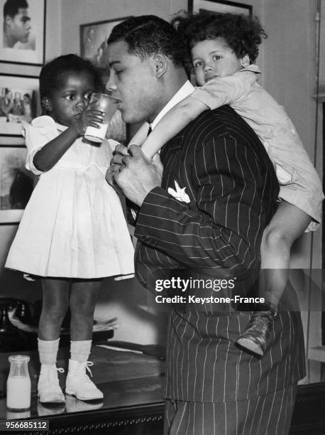 La petite Rhonetta Morris donne à boire un verre de lait au champion du monde poids lourds Joe Louis tandis qu'il porte sur son dos le petit James,...