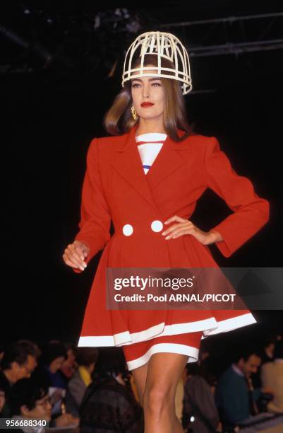 Portrait du mannequin Tatjana Patitz coiffée d'un chapeau-cage excentrique sur un tailleur jupe-veste rouge au défilé de haute-couture Guy Laroche...