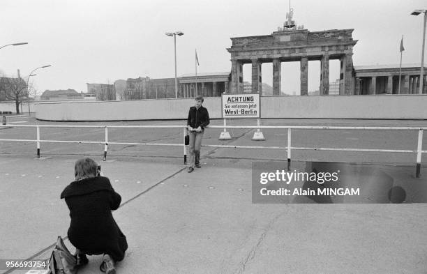 Un touriste se fait prendre en photo devant la Porte de Brandeburg près du mur de Berlin en avril 1980, Allemagne.