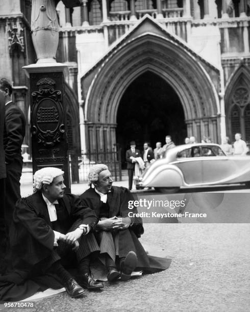 Les acteurs Ian Carmichael et Miles Malleson en tenue d'avocats se reposent entre deux prises assis sur le trottoir devant le Palais de Justice, à...