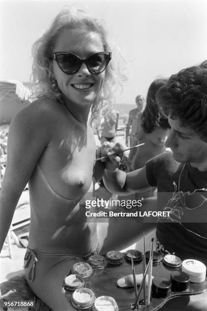 Une jeune femme se fait peindre le corps sur une plage de St-Tropez en juillet 1980, France.