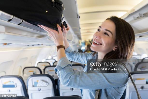 woman places luggage in airplane's overhead compartment - carry on bag stock pictures, royalty-free photos & images