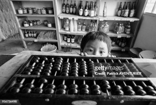 Enfant se cachant derrière le comptoir d'un magasin à Pékin en juin 1987, Chine.