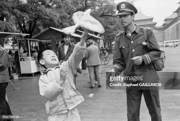 Un jeune garçon lance un oiseau cerf-volant sous l'oeil d'un policier à Pékin le 5 juin 1988, Chine.