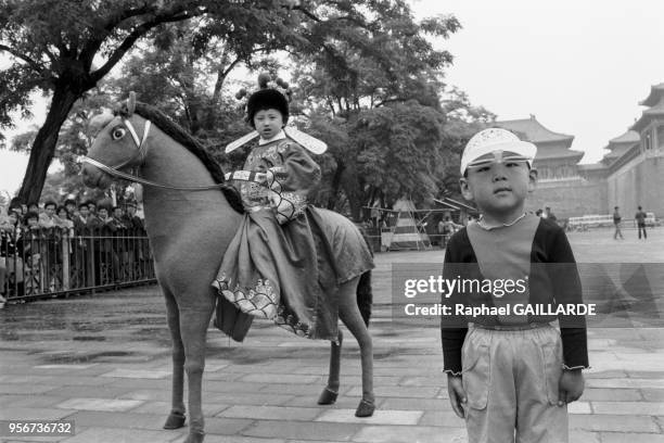 Petite fille sur un faux cheval dans un arc de Pékin le 5 juin 1988, Chine.