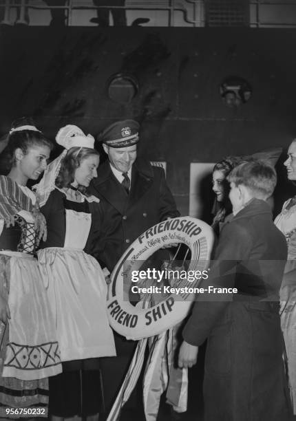 Un jeune Havrais, entouré de jeunes filles en costume régional, offre une bouée symbolique au commandant du navire 'American Leader' qui a transporté...