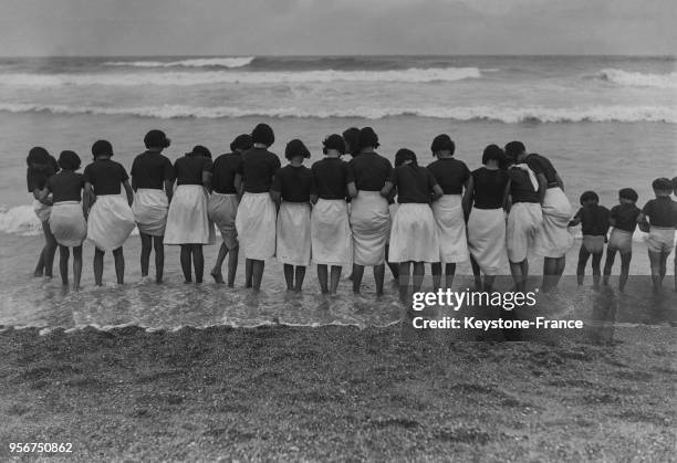 Groupe de jeunes filles en colonie scolaire trempent leurs pieds dans la mer, à Biarritz, France en août 1934.