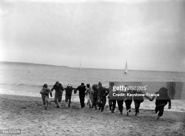 Sur la plage, de joyeux cortèges déguisés courent sur le sable, à Cannes, France en février 1933.