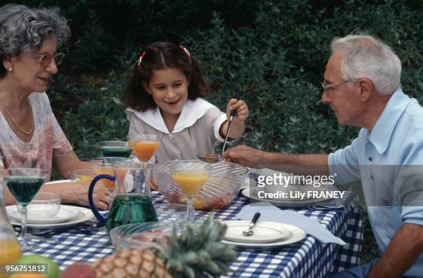 Petite fille avec ses grands parents lors d'un repas de famille dans un jardin à Créteil, en 1995, dans le Val-de-Marne, France.