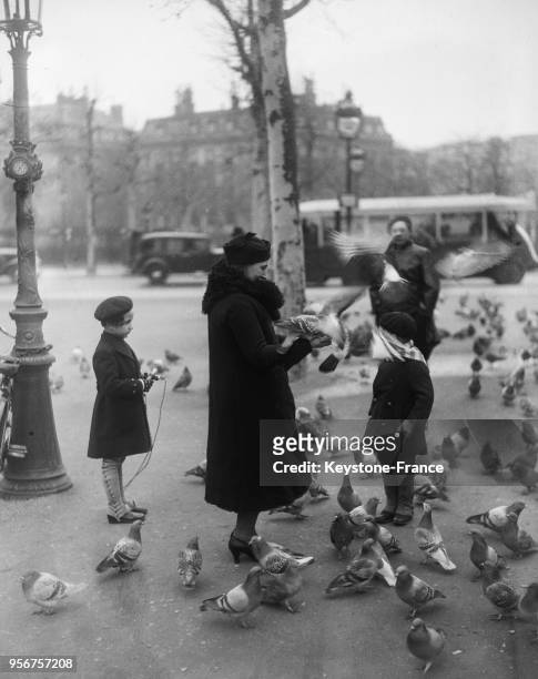 Une femme et ses enfants donnent à manger à des pigeons place de l'Etoile à Paris, France en février 1935.