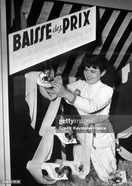 Dans une parfumerie, une vendeuse, après avoir affiché la baisse, change les prix sur les flacons de parfum, à Paris, France en 1946.