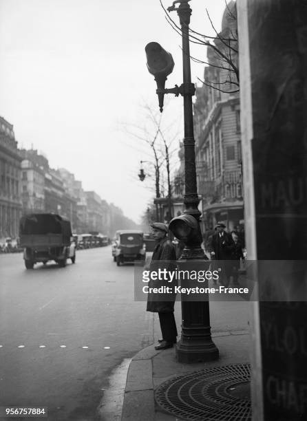 Un piéton attend l'arrêt de la circulation au feu rouge pour traverser la rue, circa 1930 à Paris, France.