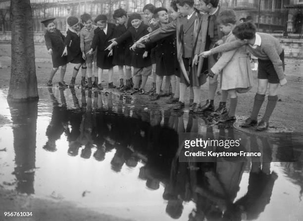 Un groupe d'enfants jouent dans le jardin des Tuileries à côté d'une flaque d'eau, à Paris, France le 6 décembre 1934.