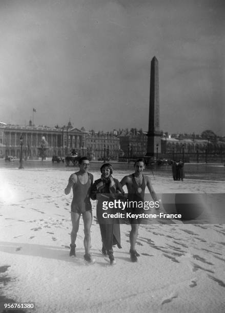 Deux hommes en tenue très légère marchent dans la neige au bras d'une femme sur la place de la Concorde, circa 1930 à Paris, France.