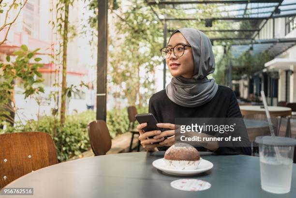 malay girl with hijab with her smartphone - malay culture stock-fotos und bilder