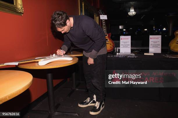 Guitarist Josh Klinghoffer of Red Hot Chili Peppers autographs a guitar after rehearsal for the Musicares Concert for Recovery at the Showbox on May...