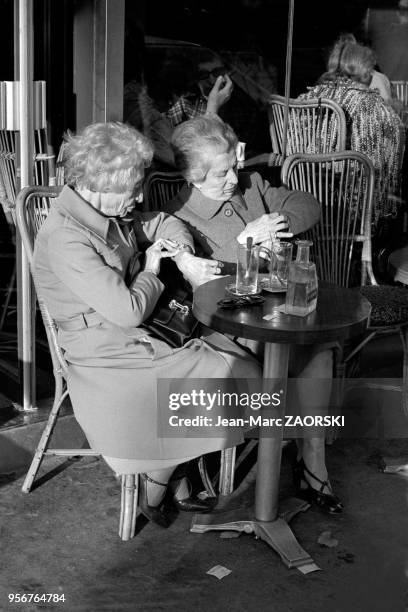 Deux femmes agées regardent leurs montres à la terrasse d'un café, rue de Passy dans le XVIe arrondissement le 3 octobre 1978, Paris, France.