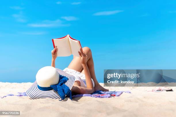 relaxing woman laying to read a book on the beach with blue sky in sunny day summer. happy travel and vacation times. - beach book reading stock-fotos und bilder