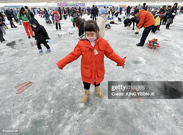 Girl casts lines through holes created in the surface of a frozen river during a contest to catch trout in Hwacheon, 120 kilometers northeast of...