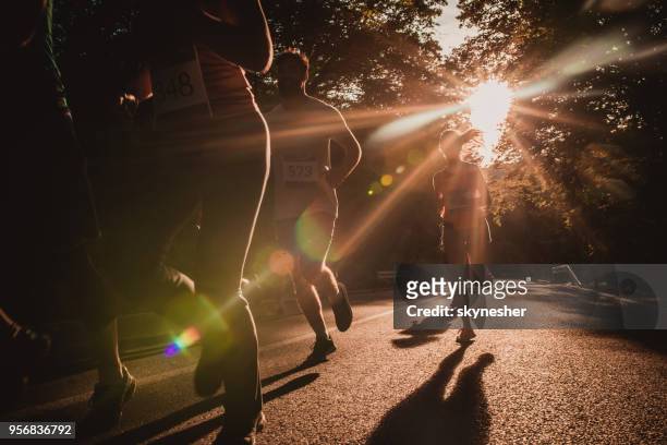 group of marathon runners racing on asphalt road at sunset. - road running stock pictures, royalty-free photos & images