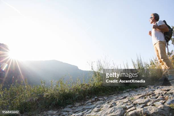 männliche wanderer hält auf gepflasterten weg zum sonnenaufgang über hügel - confidence male landscape stock-fotos und bilder