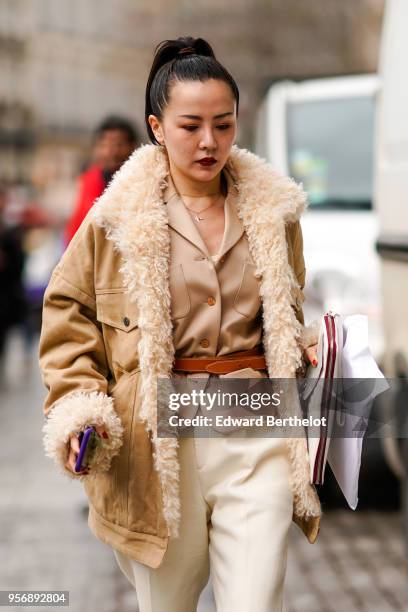 Guest wears a brown coat with sheep wool inner lining, a beige jacket, white pants, outside Louis Vuitton, during aris Fashion Week Menswear Fall...