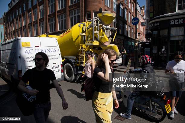 Busy street scene on Wardour Street in Soho as vehicles and pedertrians pass at the the same time including a yellow concrete mixer, which is...