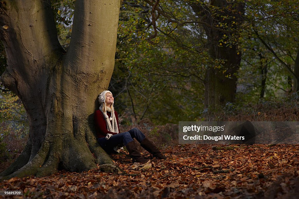 Young woman sitting against tree trunk.