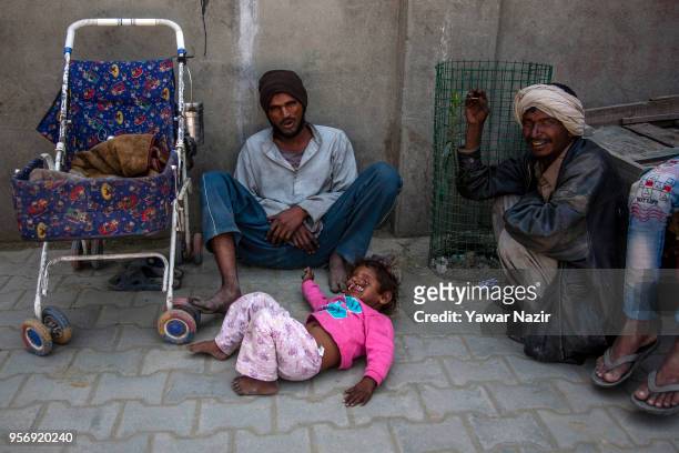 An Indian child beggar Arjun, 3 years old with the disfigured face, begs with his father on a roadside on May 10, 2018 in Srinagar, the summer...