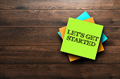 Let's Get Started, the phrase is written on multi-colored stickers, on a brown wooden background. Business concept, strategy, plan, planning.