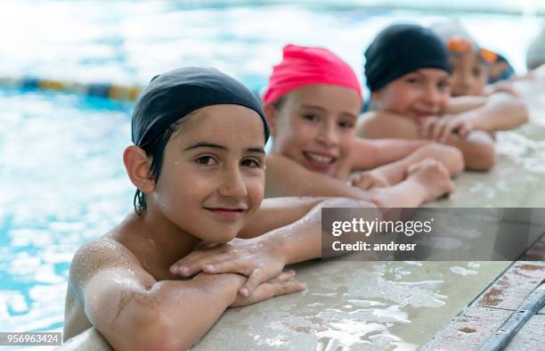 cute kids leaning on the edge of the pool all looking at camera smiling very happy - boy swimming pool goggle and cap stock pictures, royalty-free photos & images