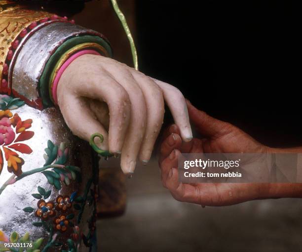 Close-up of the hand of a Buddha statue, sculpted from yak butter, as a monk holds one of its fingers at the Ta'er lamasery, Xining, Qinghai...