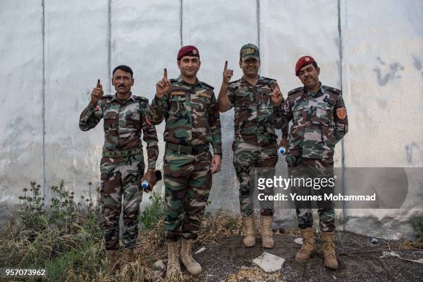 Members of the Iraqi security forces hold up an ink-stained fingers during early voting for Iraq's parliamentary elections on May 10, 2018 in Erbil,...
