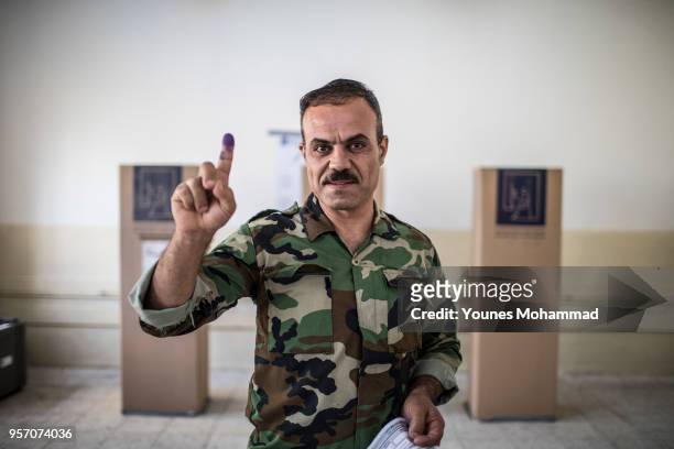Member of the Iraqi security forces holds up an ink-stained finger during early voting for Iraq's parliamentary elections on May 10, 2018 in Erbil,...
