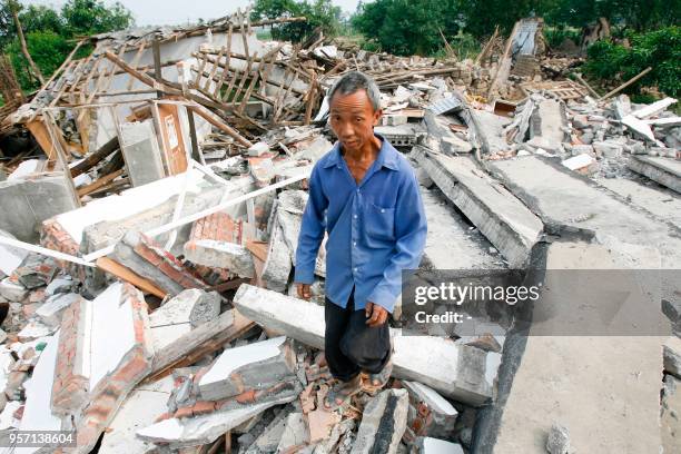 This photo taken on May 22, 2008 shows Xie Zhigui, then 52 years old, walking on the ruins of his house, damaged in the 2008 Sichuan earthquake, in...