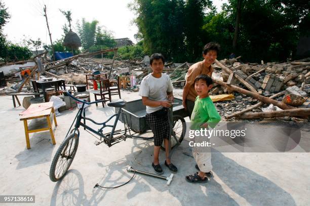 This photo taken on May 22, 2008 shows Yang Jian , then 52 years old, sitting on a bicycle with his neighbours after his house was damaged in the...