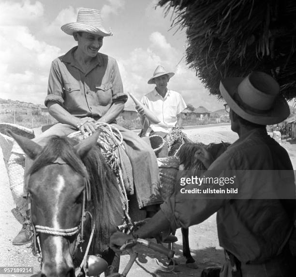 An der Straße am Anfang eines Dorfes in der Nähe von Santiago de Cuba tauschen Reiter und ein Dorfbewohner Neuigkeiten aus, aufgenommen 1962.