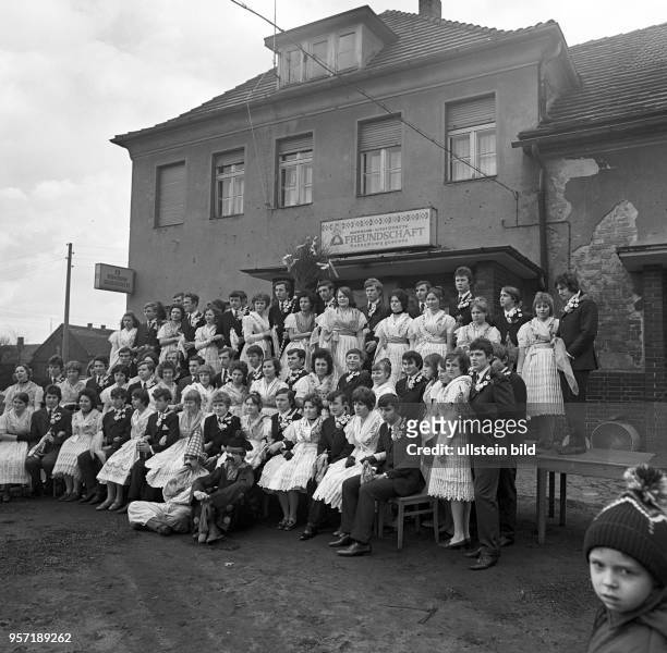 In Trachten und Anzug stehen junge Frauen und Männer am vor der Konsum-Gaststätte im Dorf Sielow bei Cottbus zum sorbischen Brauch Zapust als Teil...