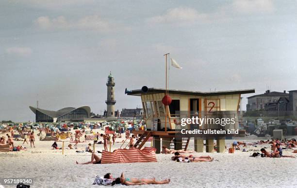 Urlauber genießen am Warnemünder Sandstrand ihre Ferien beim Baden und Sonnen, ein Rettungsschwimmer des Wasserrettungsdienstes steht für den Notfall...