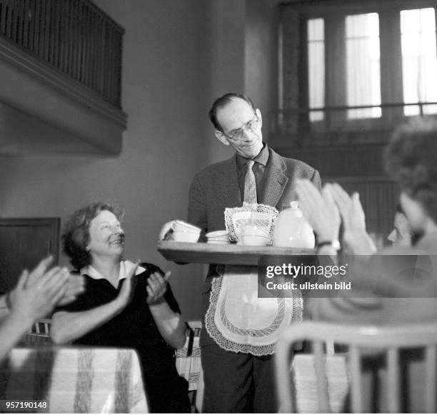 Das für eine Illustrierte gestellte Foto zeigt einen Mann mit Schürze, der einer Gruppe applaudierender Frauen eine Tablett mit Kaffeegeschirr...