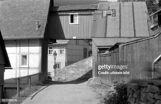 Eine menschenleere kleine Straße und alte, teils mit Dachappape gedeckte Häuser im Erholungsort Manebach in Thüringen, aufgenommen um 1960. Zu den...
