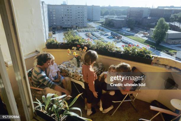 Kleines Glück auf dem Balkon - Familie Vogler hat den Tisch gedeckt, Nelken stehen in einer Vase, Vater und Mutter sitzen in Campingsesseln auf dem...