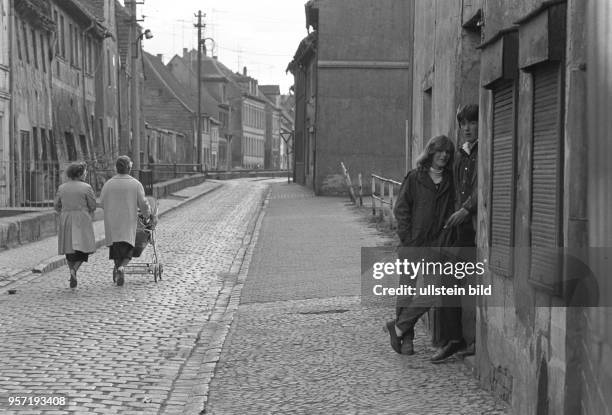 Passanten auf einer von alten Häusern gesäumten Straße in der Lutherstadt Eisleben , aufgenommen im Mai 1982. Im Vordergrund ein junges Paar in einem...