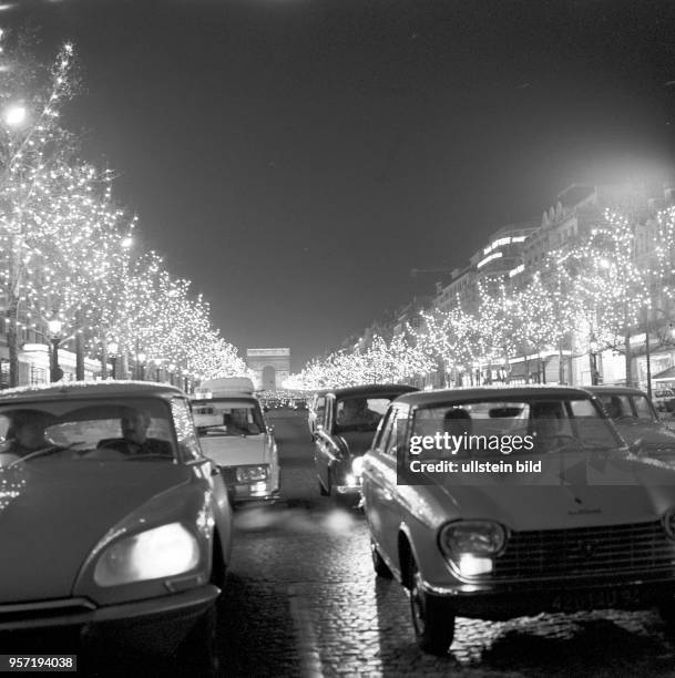 Abendlicher Verkehr auf der beleuchten Champs-Élysées in Paris, aufgenommen im November 1970. Am Ende der Avenue ist der Triumphbogen zu erkennen.