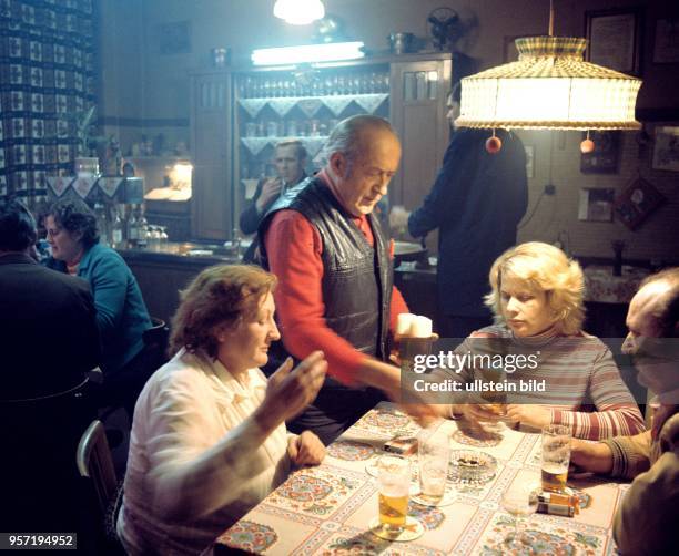 Gäste an einem Tisch in der Kneipe "Zum Löwen" bekommen vom Wirt ein Bier serviert, undatiertes Foto von 1976. An der Lampe über dem Tisch hängen...