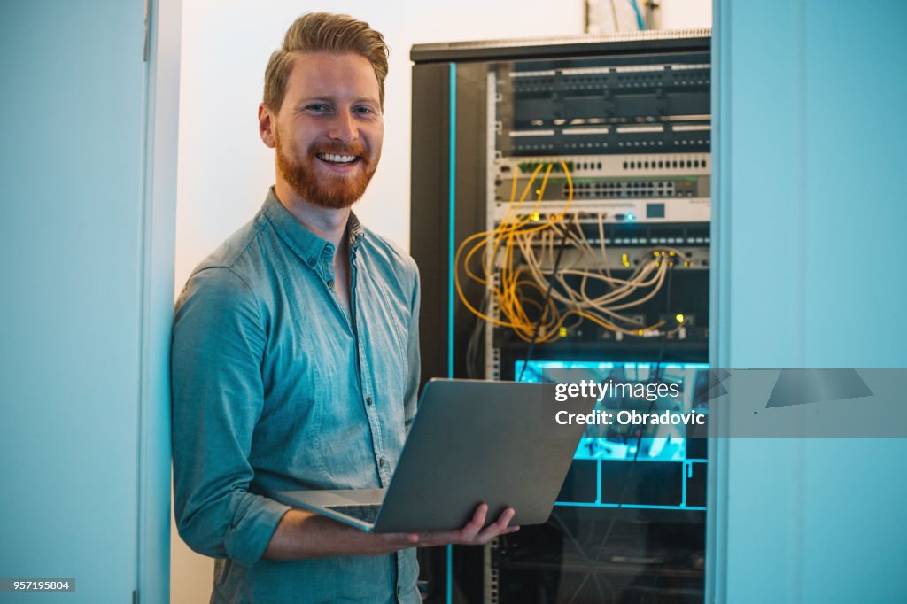 Male Caucasian IT technician using laptop in server room