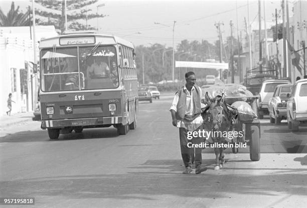 Traidition und Moderne - ein Bus und ein Mann mit einem kleinen Esel-Gespann auf einer Straße in der libyschen Hauptstadt Tripolis, aufgenommen im...